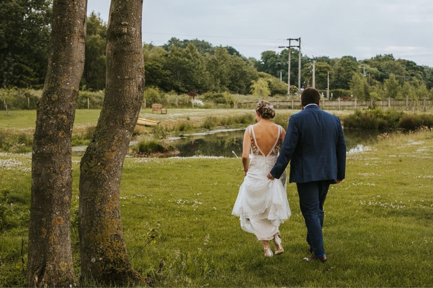 Bride and groom on grounds at Tennants, walking toward the pond